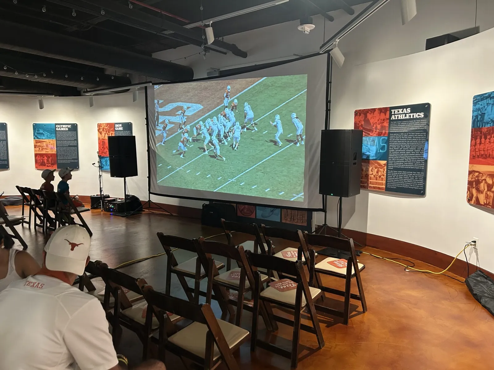 Projector and large screen at a watch party with rows of seating
