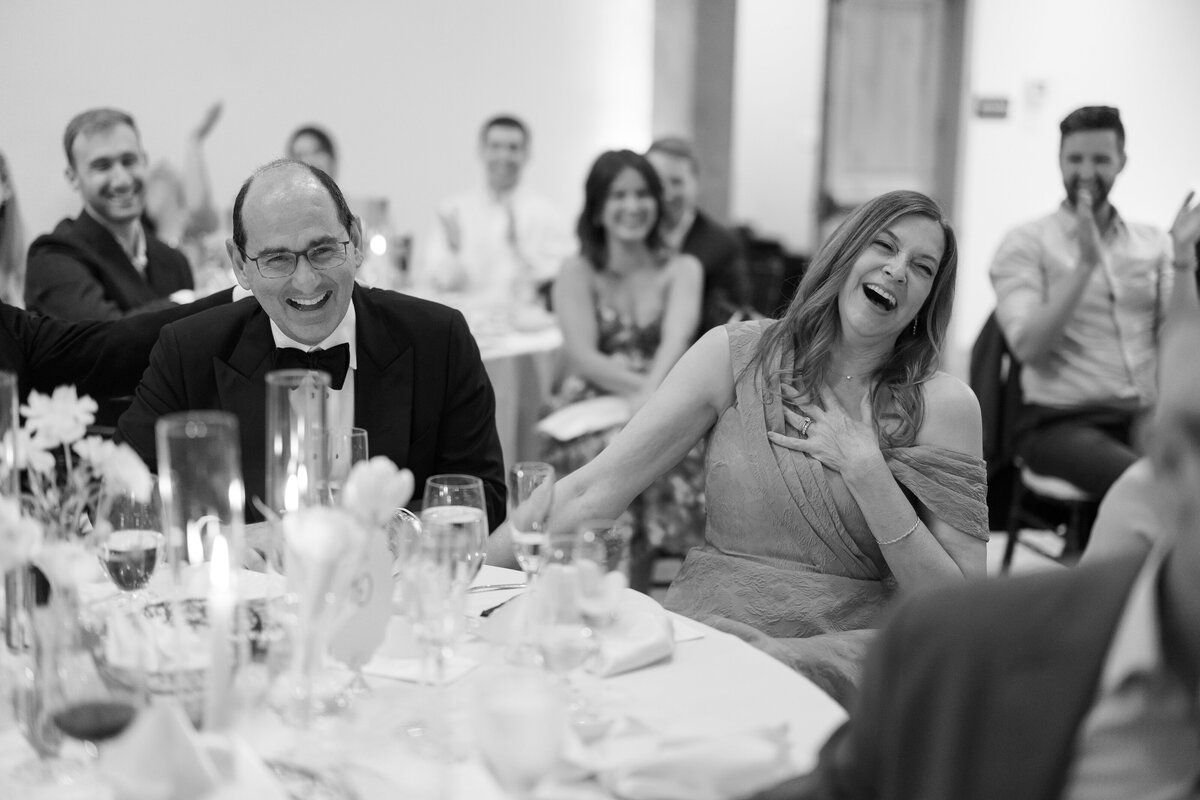 Black and white candid of wedding guests laughing during the toasts