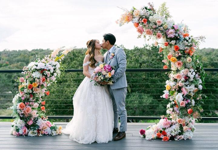 Couple kissing between floral arch pillars by Where Love Blossoms